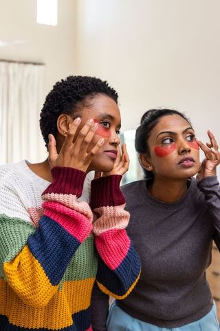 Friends applying red under-eye gel patches during at-home skincare routine