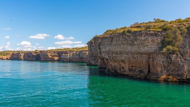 Stratified limestone cliffs bordering turquoise sea with coastal caves and rugged outcrops