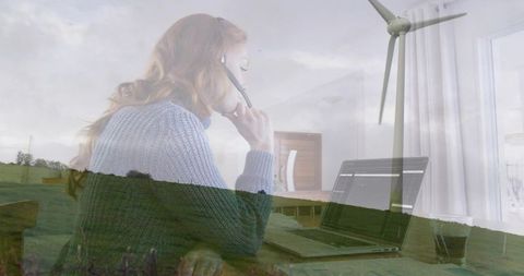 Remote worker wearing knit sweater, headset, typing at home desk with wind turbine overlay