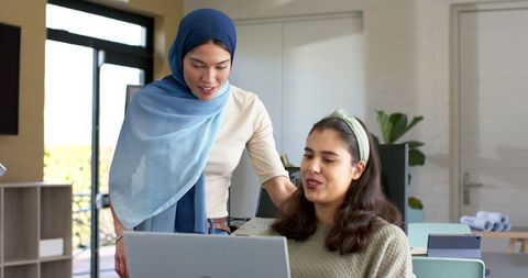 Two women collaborating on laptop in bright office mentoring and planning together