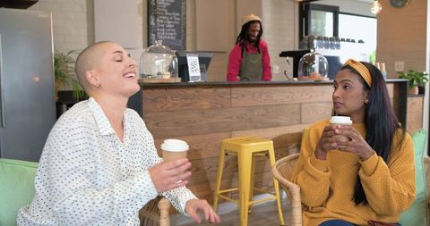 Diverse friends laughing and enjoying takeaway coffee in cozy cafe with wooden counter