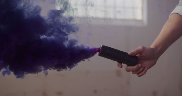 Person holding a smoke flare emitting purple smoke, with copy space. Captured indoors, the vibrant smoke adds a dynamic touch to the scene.