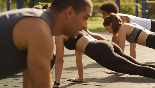 Sunlit outdoor group practicing plank exercise on rubber tiles for core strength training