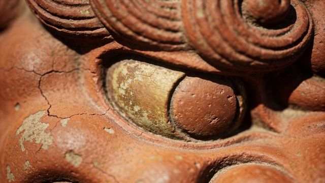 Weathered terracotta relief close-up showing cracked clay texture, coiled ridge detail