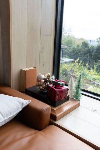 Cozy holiday corner with tan leather sofa, gift boxes, glass ornaments and garden view