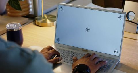 African male typing on laptop with blank screen crosshair markers in modern workspace