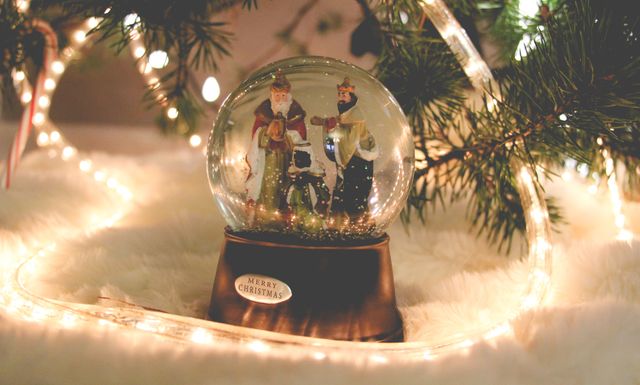 An ornate snow globe featuring Santa Claus and two figures stands on a fluffy white surface surrounded by glowing string lights. Ideal for holiday greeting cards, festive decor catalogs, and blog posts highlighting holiday season decorations and cozy settings.