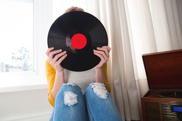 Woman hiding her face with vinyl record at home