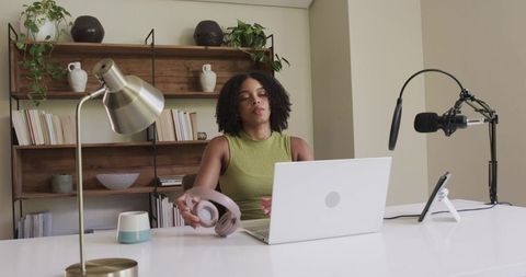 African american woman prepping podcast in home office with laptop, microphone, headphones