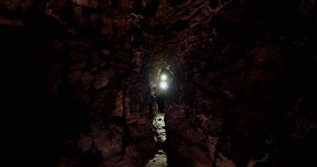 Torch lights through crack in rock formations of dark natural cave system, copy space. Geology, exploration, caving, nature and underground.