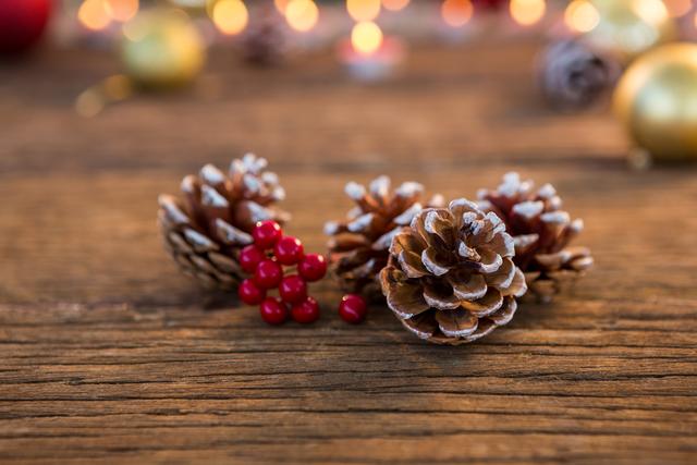 Pine cone with fake snow and cherry on wooden plank during christmas time