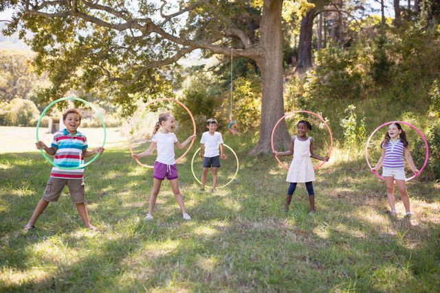 Group of cheerful friends playing with hula hoops on grassy field at campsite