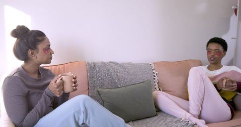Relaxed diverse friends with coffee and gel masks on sofa