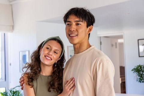 Multicultural young couple smiling and embracing in sunlit modern living room cozy moment