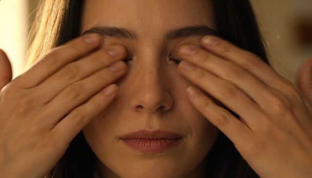 Adult woman covering closed eyes with hands in warm soft light for calm introspection
