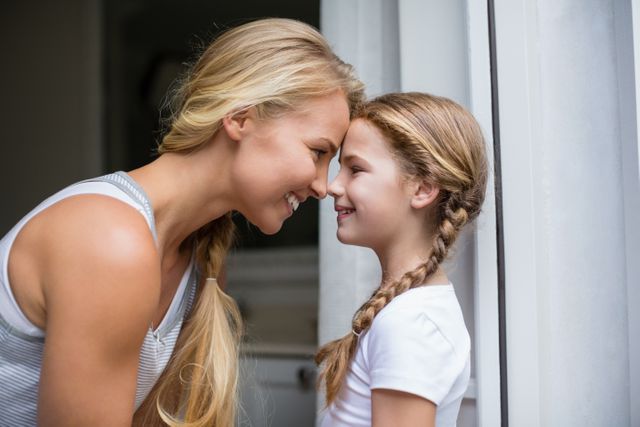 Mother and daughter sharing a tender moment, smiling and looking into each other's eyes. Perfect for illustrating family bonds, parenting, love, and happiness. Ideal for use in family-oriented advertisements, parenting blogs, and social media posts celebrating family connections.