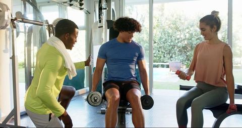 Young Couple Lifting Weights with Trainer Assisting in Modern Gym