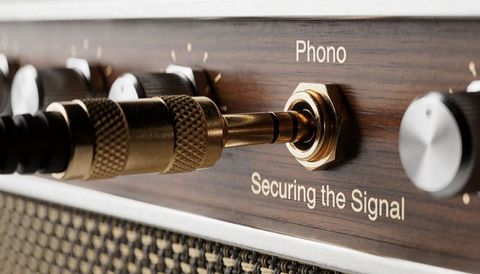 Vintage brass knurled plug connecting to phono jack on wood-veneer hi-fi amplifier