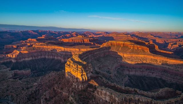 Drone capturing golden light on sandstone butte and layered desert canyon at sunrise
