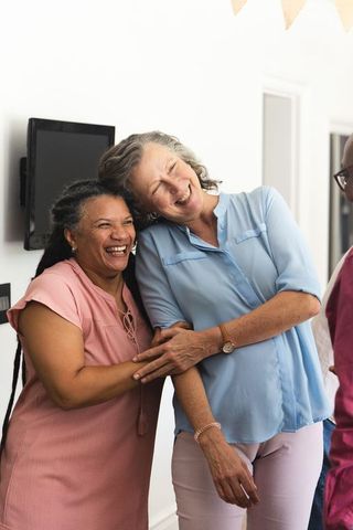 Mature friends laughing together in sunlit home interior, candid companionship and joy