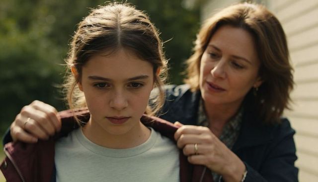 Mother adjusting teen daughter's maroon jacket in garden embracing quiet family moment
