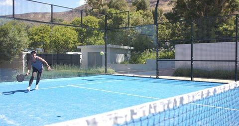 Female athlete lunging and returning padel ball on bright blue outdoor court under sun