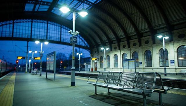 Empty train station platform at dusk featuring metal benches under arched glazed canopy