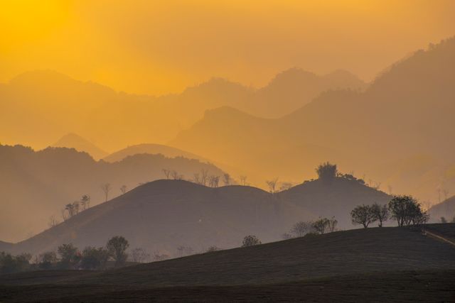 Capturing a stunning view of a golden sunset illuminating the misty hills and distant layers of mountains. Ideal for use in travel blogs, nature calendars, scenic postcards, landscape photography portfolios, and serene wallpaper backgrounds.