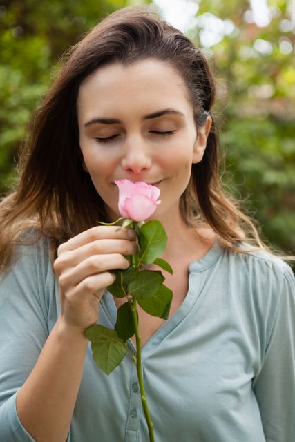 Beautiful woman with eyes closed smelling pink rose at garden