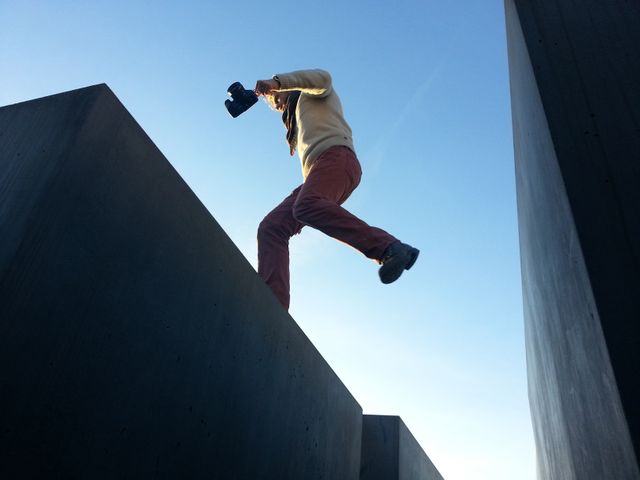 Photographer jumping between large concrete blocks while holding a camera in an urban setting. Could be used to portray adventure, photography hobby, or urban exploration themes.
