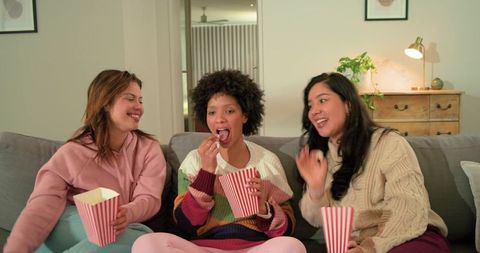 Friends enjoying cozy movie night on couch sharing popcorn and laughter during girls night