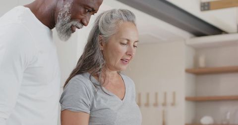African american man and caucasian woman standing in modern kitchen looking at countertop