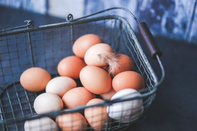 Showing a wire basket filled with fresh farm eggs and a small feather. Great for illustrating organic lifestyles, farm-to-table food concepts, and rustic kitchen decor ideas.
