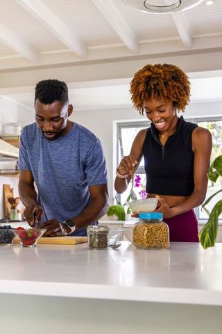 Couple preparing breakfast at bright kitchen island, chopping berries and stirring