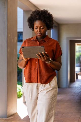 African american professional woman using tablet while walking in modern covered walkway