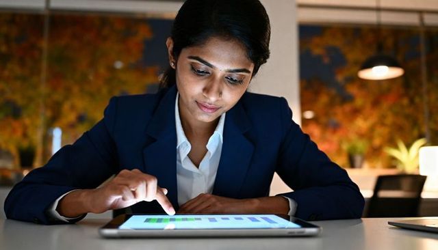 Indian businesswoman analyzing tablet dashboard at modern office desk, working late