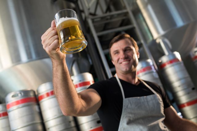 Low angle view of smiling worker holding beer glass at warehouse