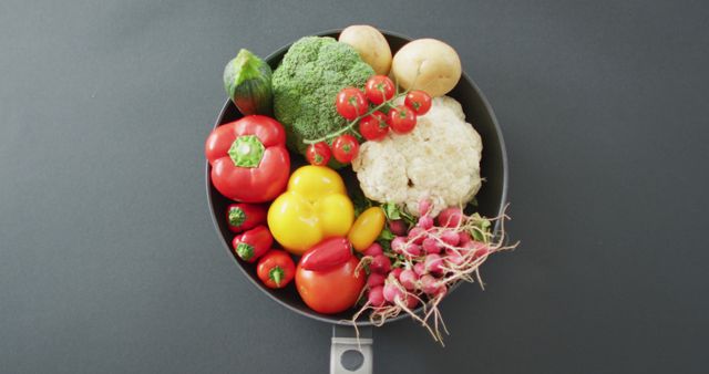Colorful assortment of fresh vegetables placed in a frying pan, ideal for promoting healthy eating, vegan recipes, organic food advertising, and cooking blogs. The mix includes tomatoes, bell peppers, cucumbers, broccoli, radishes, cauliflower, and potatoes, offering a vibrant visual for culinary themes and health-focused content.