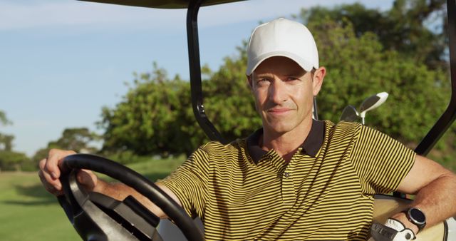 Portrait of happy caucasian male golf player with white cap riding golf cart at golf course. Golf, sport and active lifestyle, unaltered.