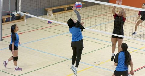 Female volleyball players jumping at net with hijab athlete spiking tricolor ball