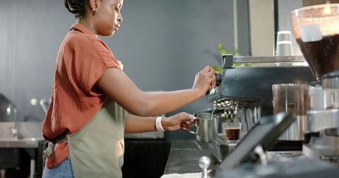 African american barista preparing espresso and steaming milk behind modern café counter