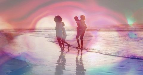 Family walking on sunset beach carrying child piggyback with pastel lens flare reflections