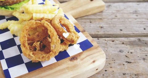 Fried onion rings and fries on rustic wooden board