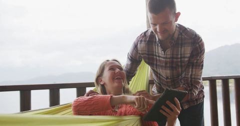 Couple Relaxing in Hammock Using Tablet at Lakeside Cabin