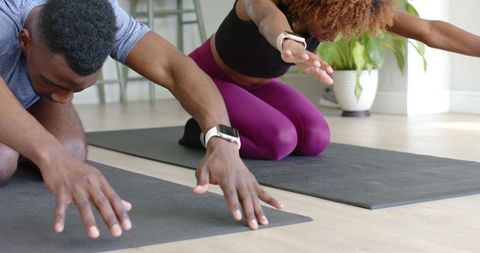 Couple stretching on yoga mats tracking fitness with smartwatches during home workout