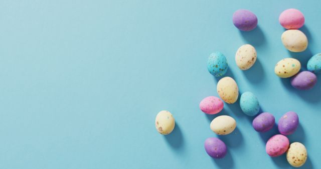 Colorful pastel Easter eggs scattered on a blue background, evoking springtime celebrations and festive decorations. Ideal for Easter greeting cards, holiday advertisements, social media posts, and spring-themed promotions.