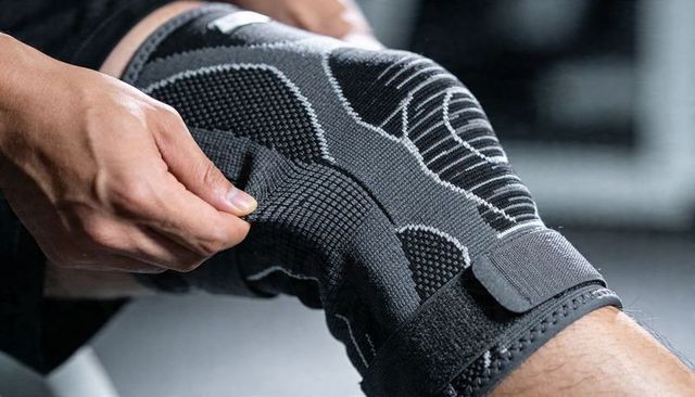 Male athlete adjusting black-gray compression knee brace with velcro strap joint support