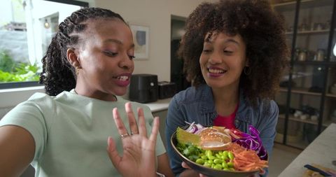 Diverse friends presenting colorful health bowl at kitchen counter smiling and sharing