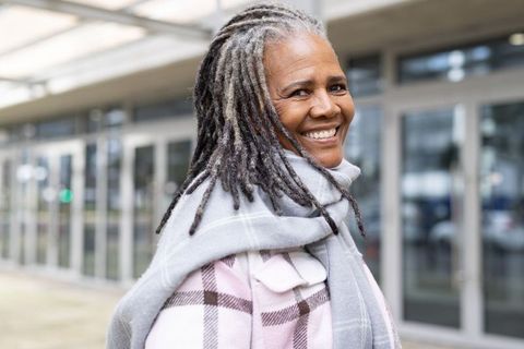 Smiling mature black woman wearing pastel plaid coat and gray scarf near modern entrance
