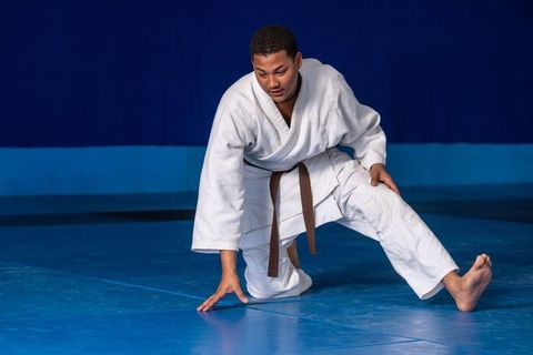 Male martial artist in gi practicing movements on blue dojo mat
